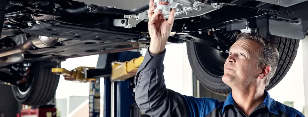 A mechanic changing oil in a car on a lift, with a fresh bottle of synthetic oil nearby