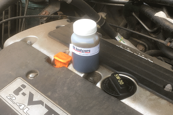 A technician holding a small bottle of used motor oil for analysis